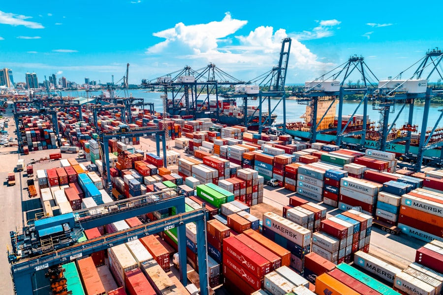 Aerial view of a container terminal, with stacked shipping containers and gantry cranes loading a vessel.